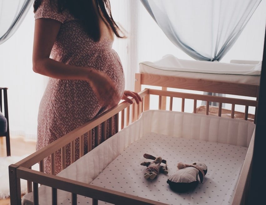pregnant woman beside an empty crib