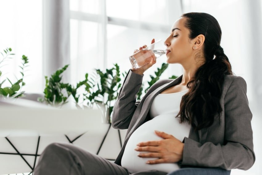 Pregnant woman sitting in office chair and drinking water