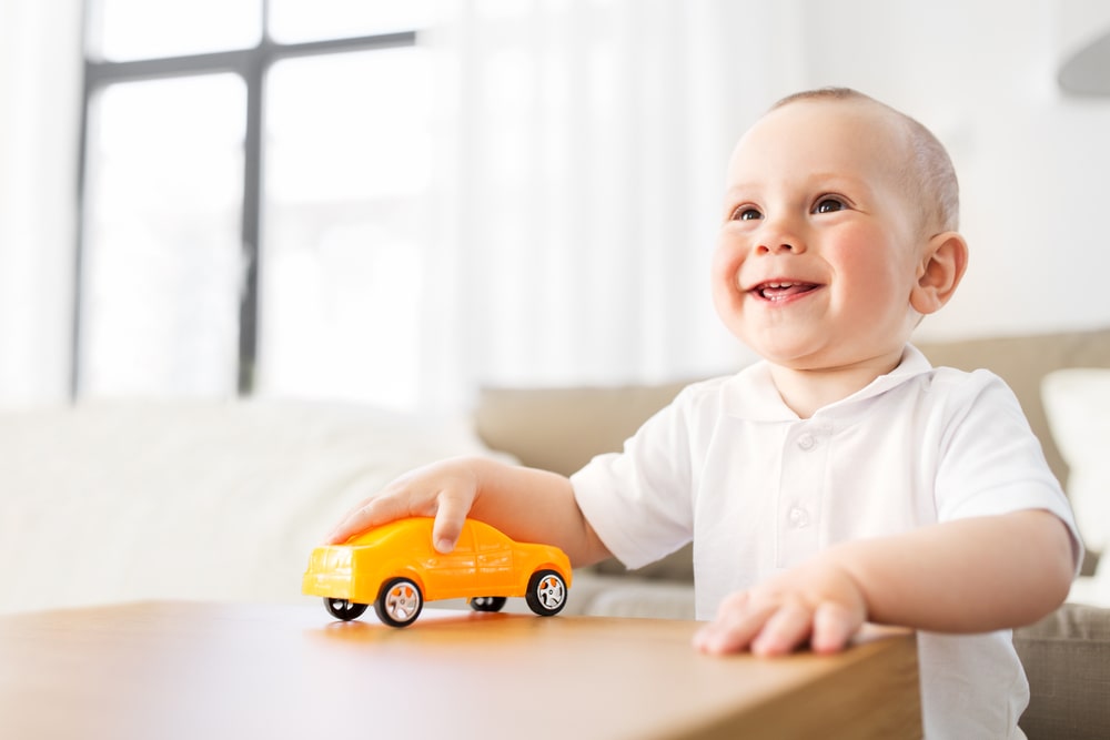 Happy baby boy playing with toy car at home