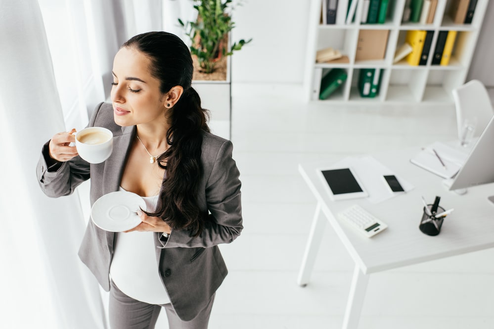 High angle view of pregnant woman standing in office and drinking coffee