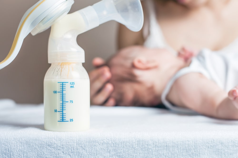 Manual breast pump with milk, mother and baby at background