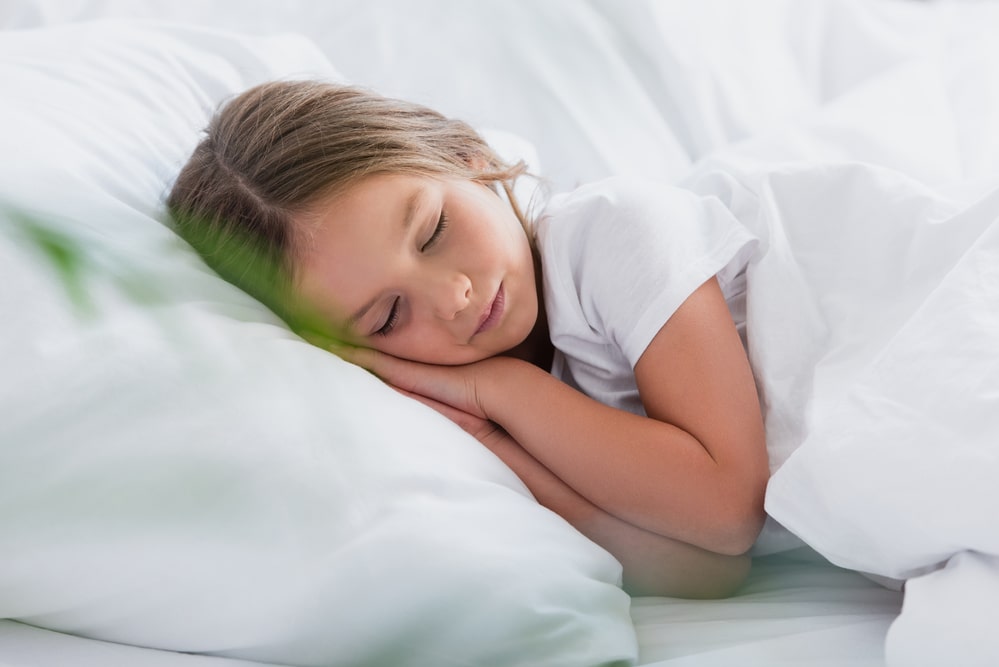 Selective focus of girl sleeping while lying on white bedding