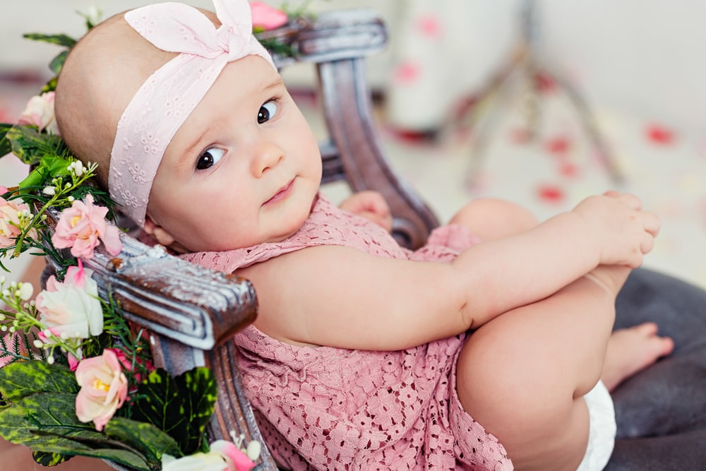Small very cute wide-eyed smiling baby girl in a pink dress