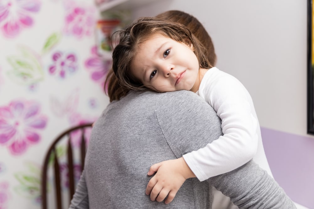 Little girl with sad expression embracing mother at home