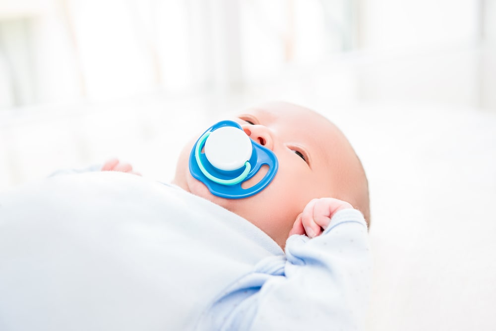 Adorable little newborn baby with pacifier lying on the bed