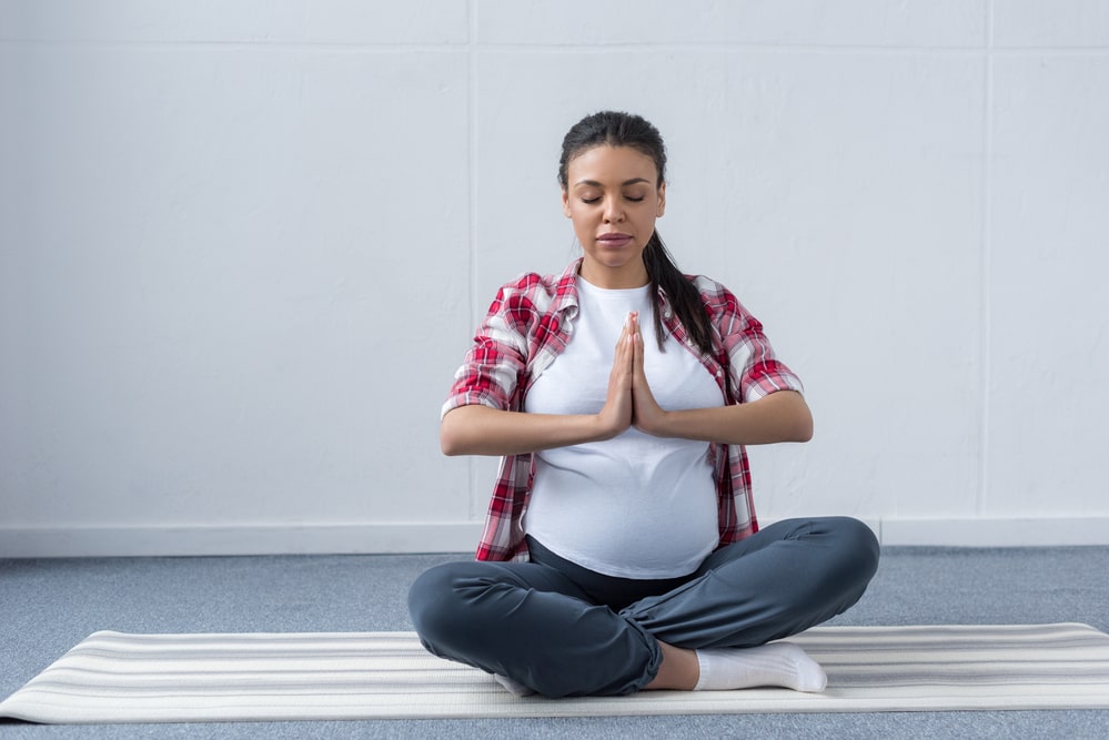 African american pregnant woman practicing yoga on mat
