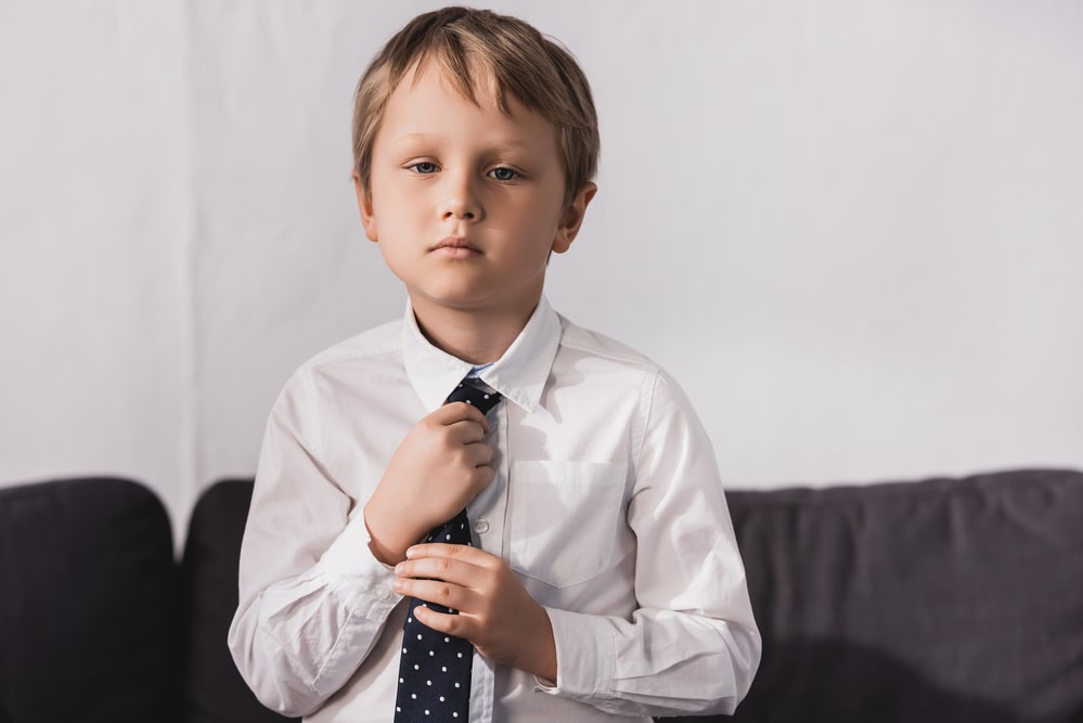 Serious boy in white shirt putting tie on and looking at camera