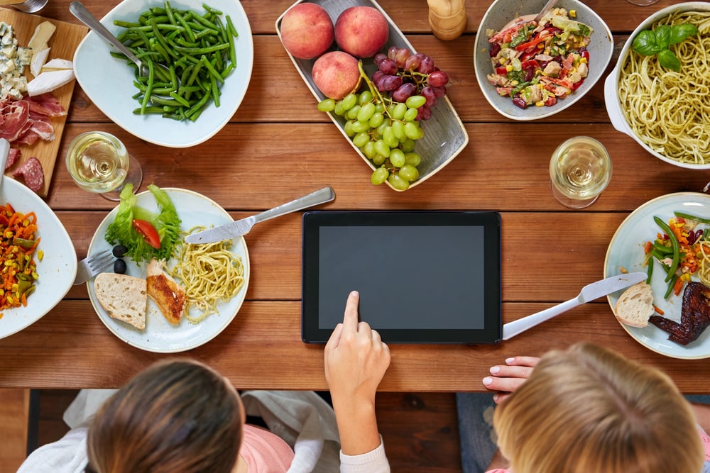 Women with tablet pc at table full of food