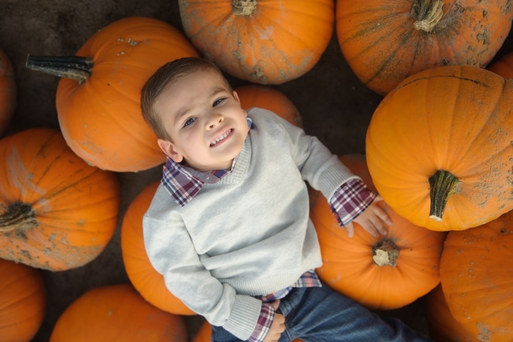little boy lying down on pumpkins smile